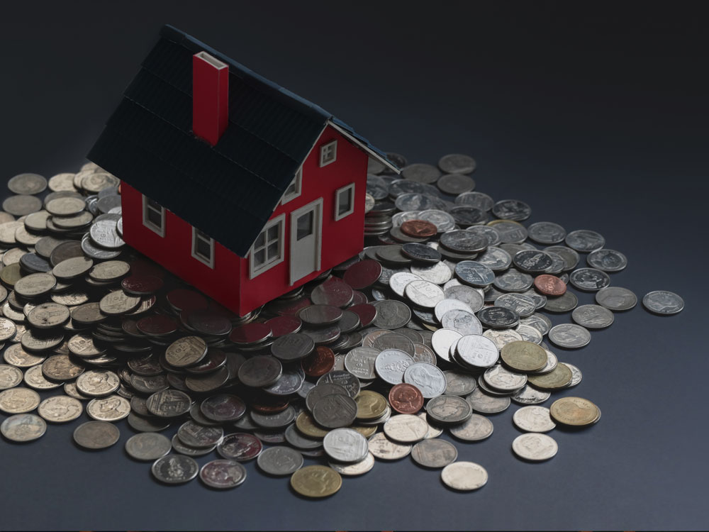 A Toy house on top of a pile of coins 