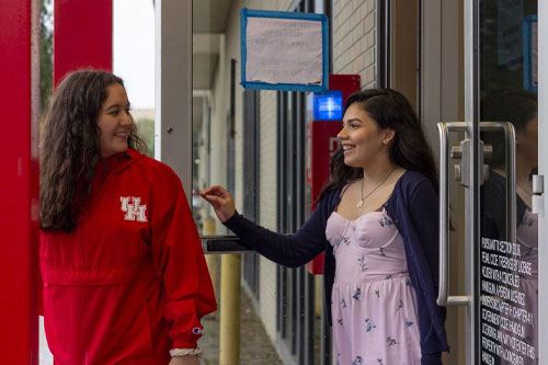 Two students comparing their notes in notebooks sitting side by side outside.