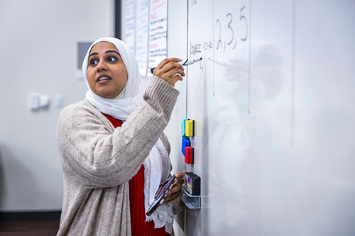 Woman with a head scarf writing on a white board