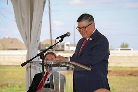 A dark grey haired man with glasses smiling while at a podium